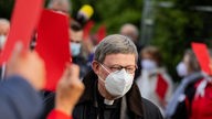  Kardinal Woelki geht mit Mund-Nasen-Schutz und gesenktem Blick zwischen Reportern hindaurch