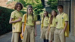 Filmszene aus "Club Zero", eine Gruppe von Jugendlichen in gelben Schuluniformen schaut zu einem Punkt hinter der Kamera.