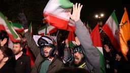 Iraner nach Angriff auf Israel: Im Hintergrund Iran und Palästina Flaggen