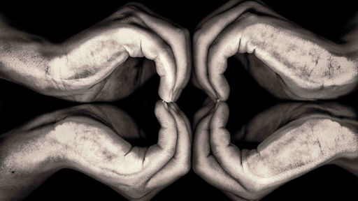 Zwei Hände formen Herzen vor schwarzem Hintergrund.