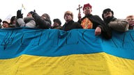 Demonstranten auf dem Maidan, hinter einem Banner, darunter auch ein Geistlicher