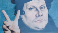 Ein Plakat  in Lutherstadt Wittenberg: Ein Portrait Luthers, collagiert davor eine hand, die das Victory-Zeichen bildet und die Unterschrift "Ich kann nicht anders"