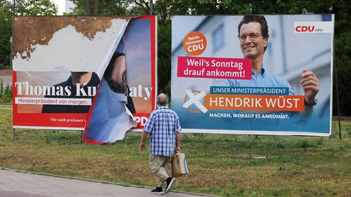 Nordrhein-Westfalen, Düsseldorf: Ein Mann geht an einem abgerissenen Wahlplakat des SPD Spitzenkandidaten, Thomas Kutschaty (l.), und einem vom Spitzenkandidaten der CDU, Ministerpräsident Hendrik Wüst vorbei.