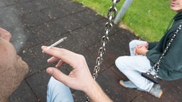 Zwei junge Männer mit Joint auf einer Spielplatzschaukel